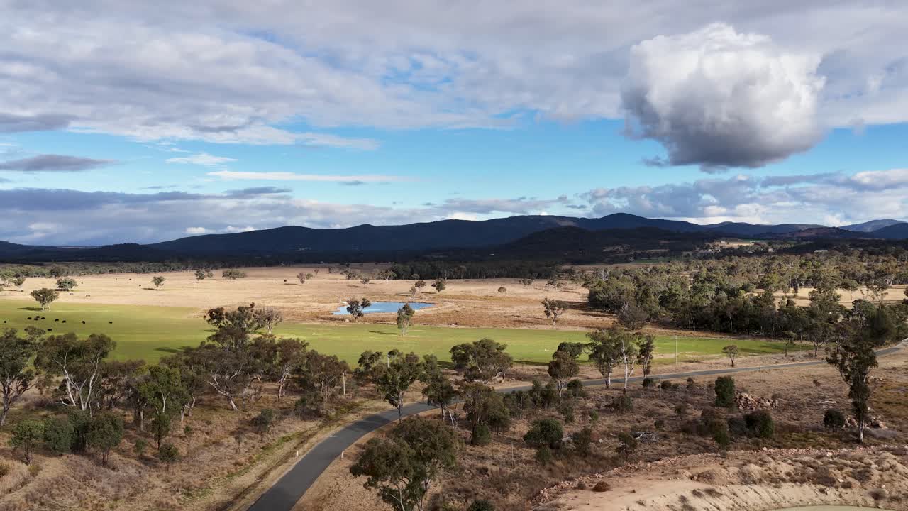 Drone camera smoothly pans across a rural Australian landscape with farm ponds, open fields, scattered trees, and distant hills under partly cloudy daylight