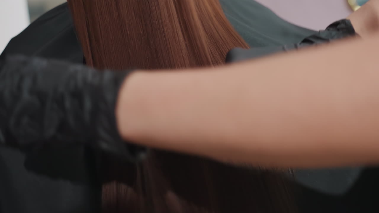 salon scene caucasian woman back receiving gloss prep, gloved stylist smoothing long straight brown hair with comb, mirror reflection, black cape, gentle precision strokes, shiny healthy finish