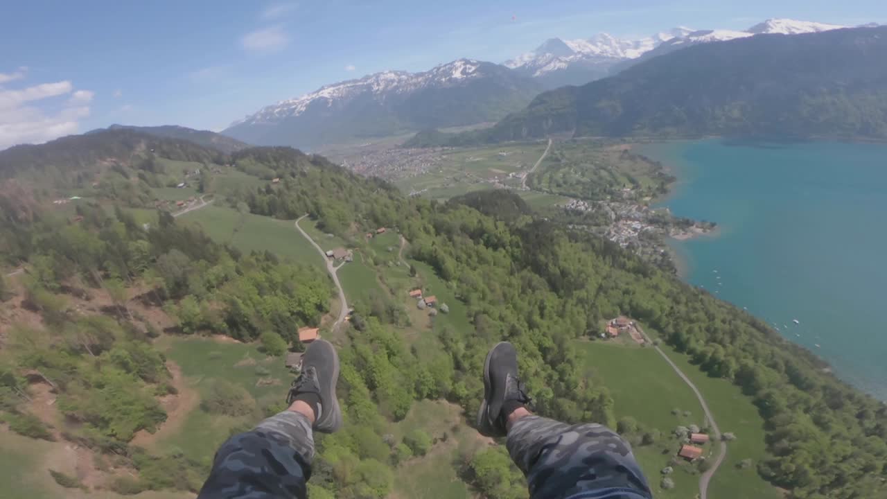 Ripresa POV di un parapendio che vola sopra la montagna lussureggiante e il lago blu calmo in Svizzera in una giornata di sole - aerea - POV