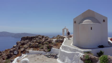 aerial: a man walks next to a church on a greek island on a sunny day