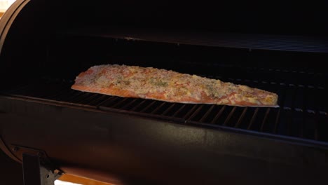 opening the lid on a smoker checking on a salmon fillet and allowing smoke to billow out while cooking on a wood pellet grill during the evening