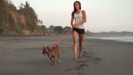 mujer joven activa corriendo con perro en la playa