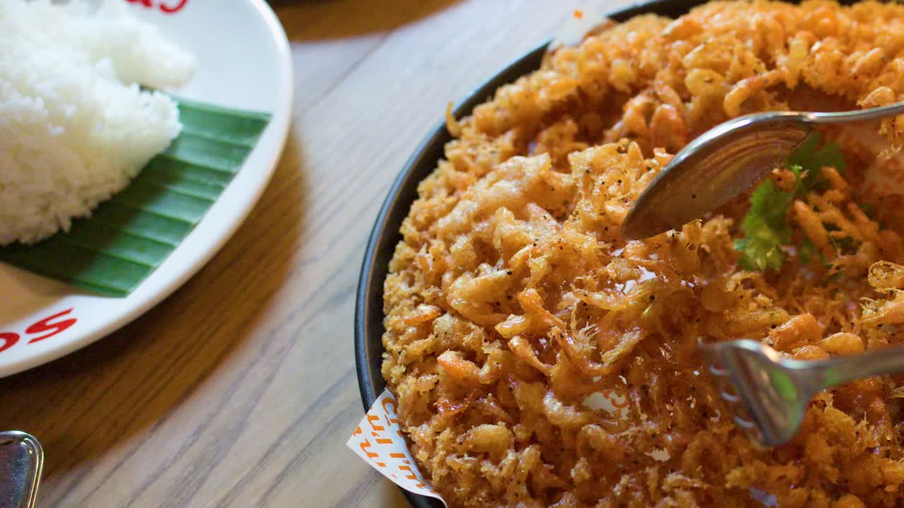 Hands use spoons to serve golden fried shrimp pancake in bright, natural light restaurant setting