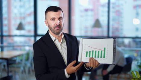 businessman makes chart presentation to the camera. smiling positive man explains the graphs actively. close up.