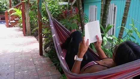 young brunette woman in tropical hammock enjoys reading a good book