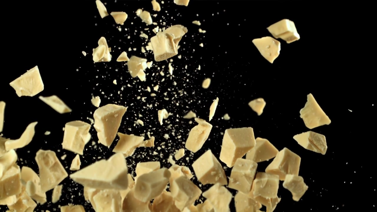 White Chocolate Chunks Falling and Scattering on Black Background in Slow Motion
