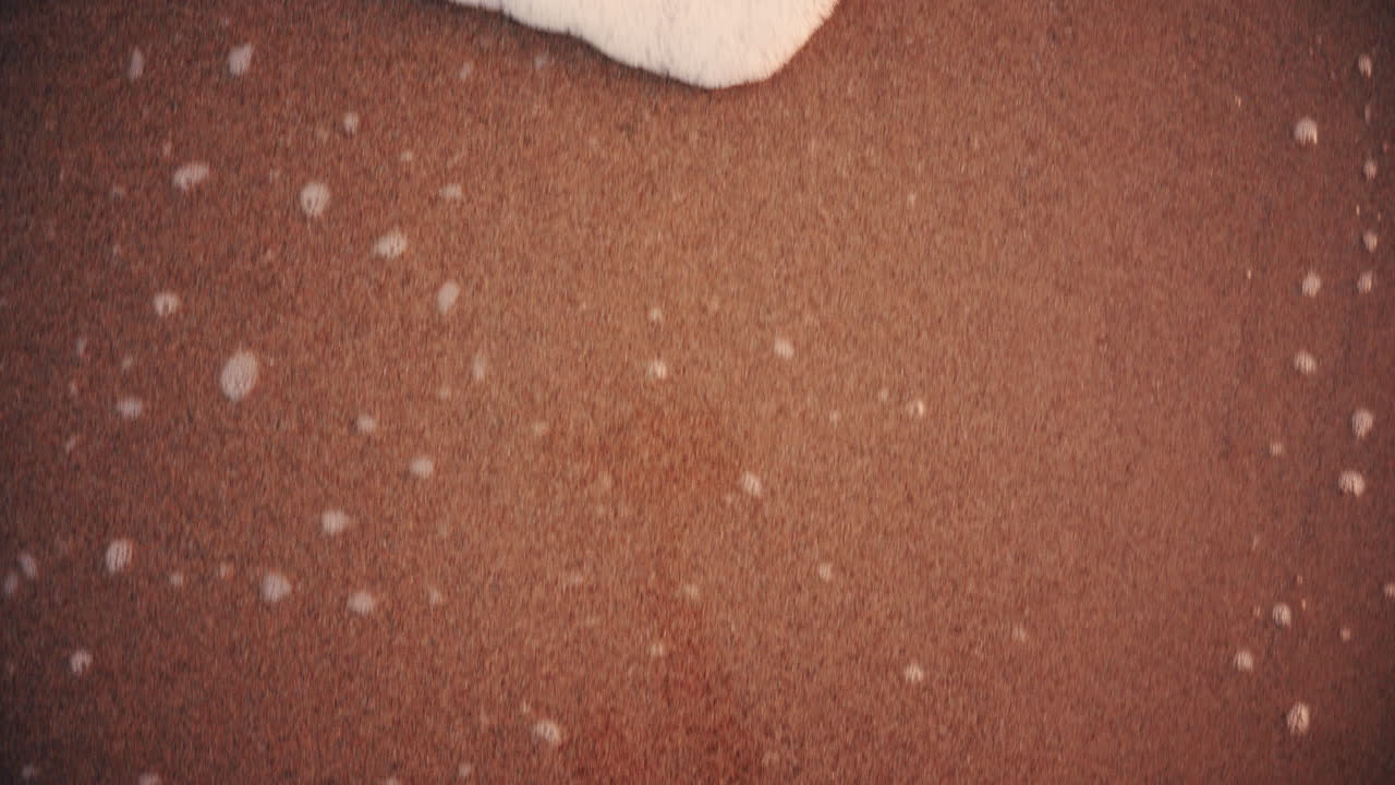 Close up of small ocean waves gently rolling onto the sandy beach at sunset
