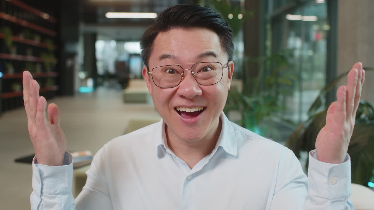 Chinese young businessman in shirt looking at camera shocked by sudden victory in office lobby