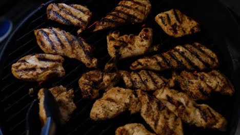 chicken being grilled on electric grill with charred meat and red heating element burner, being flipped by hand with red painted fingernails, and tong grabber