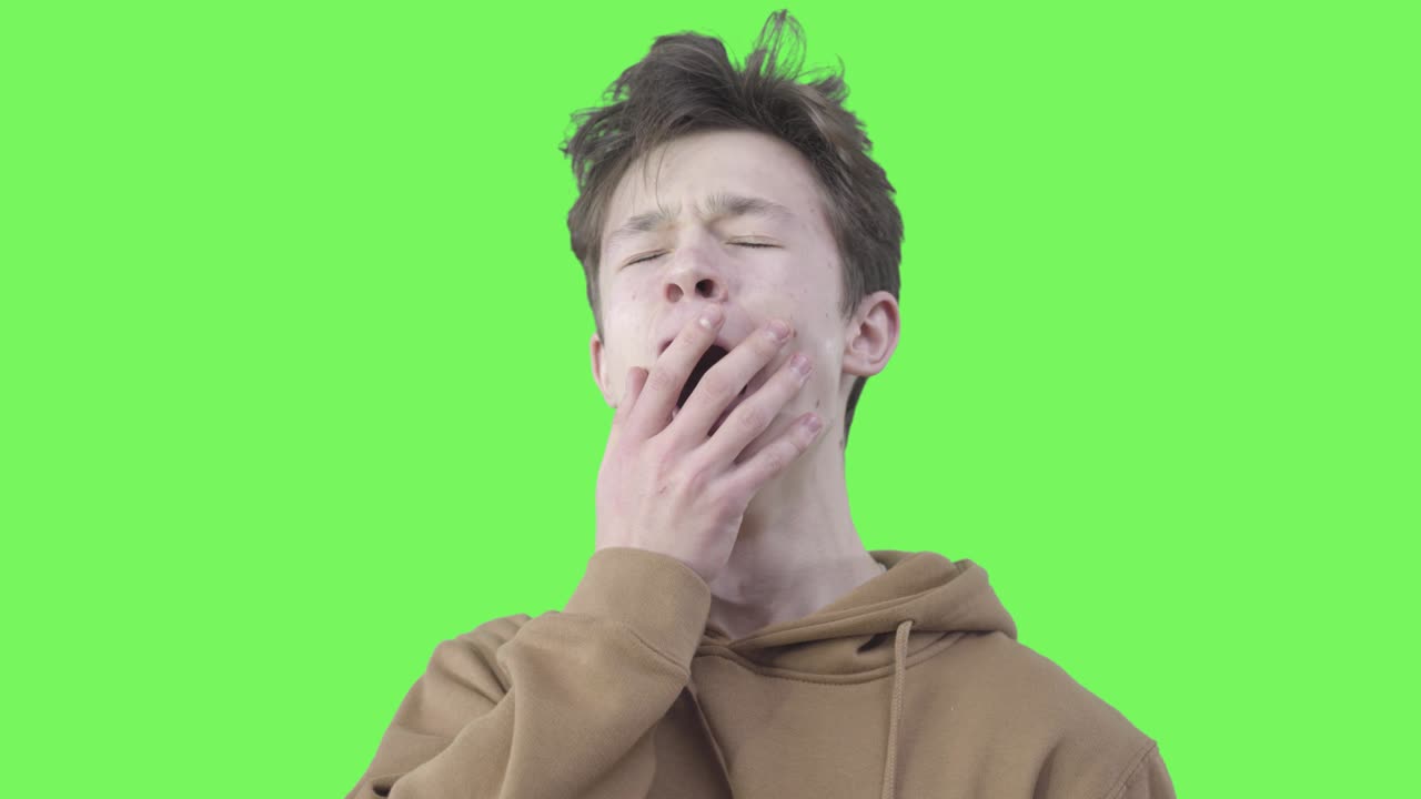 primer plano de un niño cansado bostezando. retrato de un estudiante universitario agotado posando en el fondo verde. agotamiento, cansancio, exceso de trabajo, estudio. chromakey.