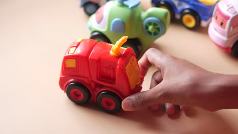 child's hand holding a red toy fire truck surrounded by other toy vehicles