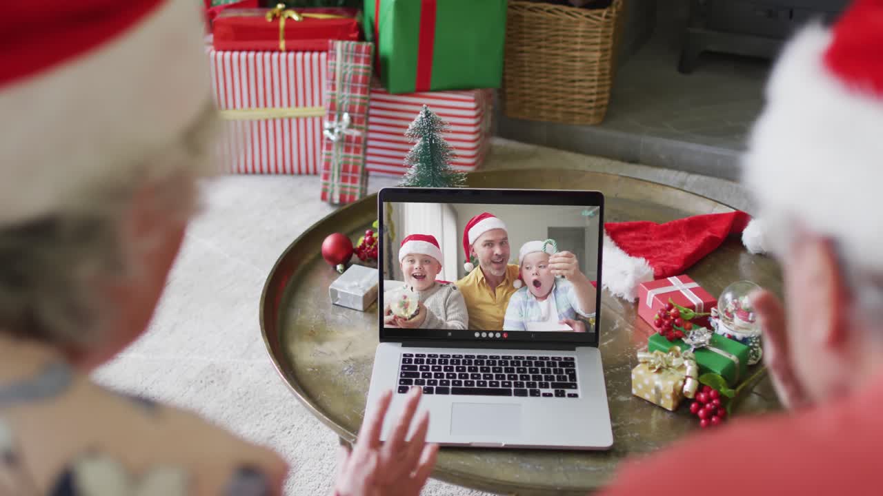 pareja de adultos mayores caucásicos con sombreros de santa usando computadora portátil para una videollamada de navidad con la familia en la pantalla