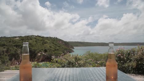 timelapse of table with fresh cold beer bottle and two chairs overlooking sea bay ocean cliff seascape clouds in the sky , holiday vacation