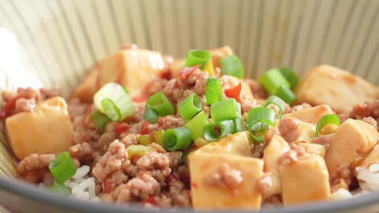 Making stir-fried mapo tofu with hot spicy sauce and scallion over white rice in a bowl at home