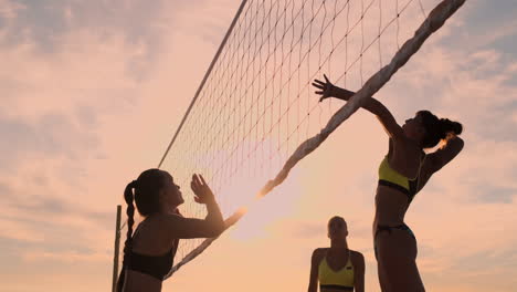 athletic girl playing beach volleyball jumps in the air and strikes the ball over the net on a beautiful summer evening. caucasian woman score a point.