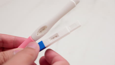 close-up of an individual holding two kinds of home pregnancy test kits, one colored blue and another one colored pink