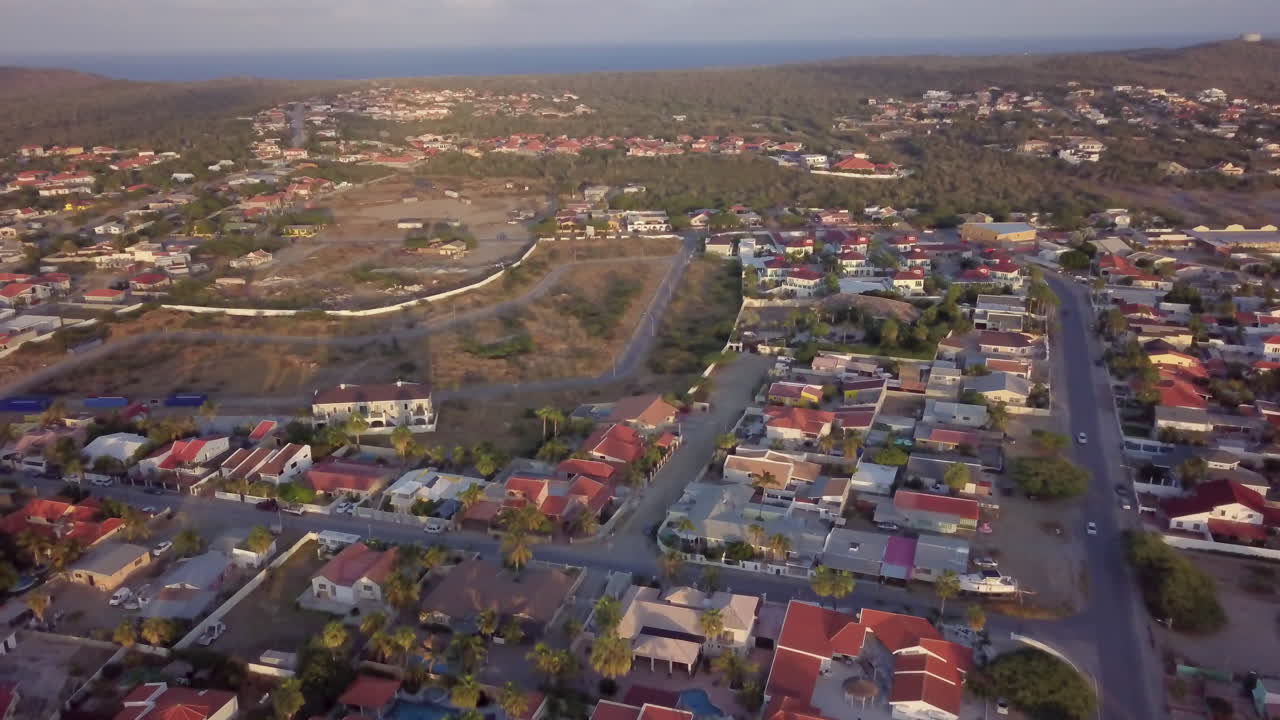 volando sobre casas tropicales en aruba con palmeras durante la puesta de sol