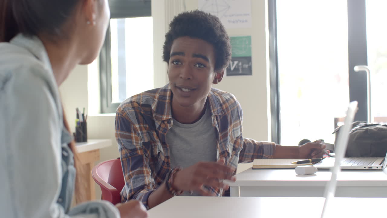 Talking to classmate, teenage boy sitting at desk in high school classroom