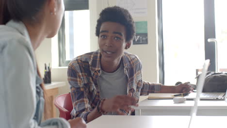 talking to classmate, teenage boy sitting at desk in high school classroom