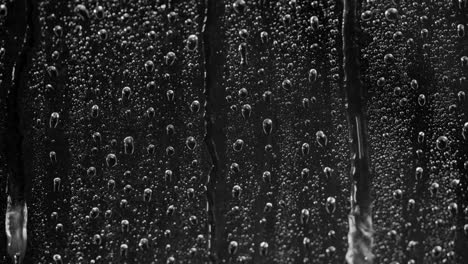 close up rain on window, water drops following down on black background