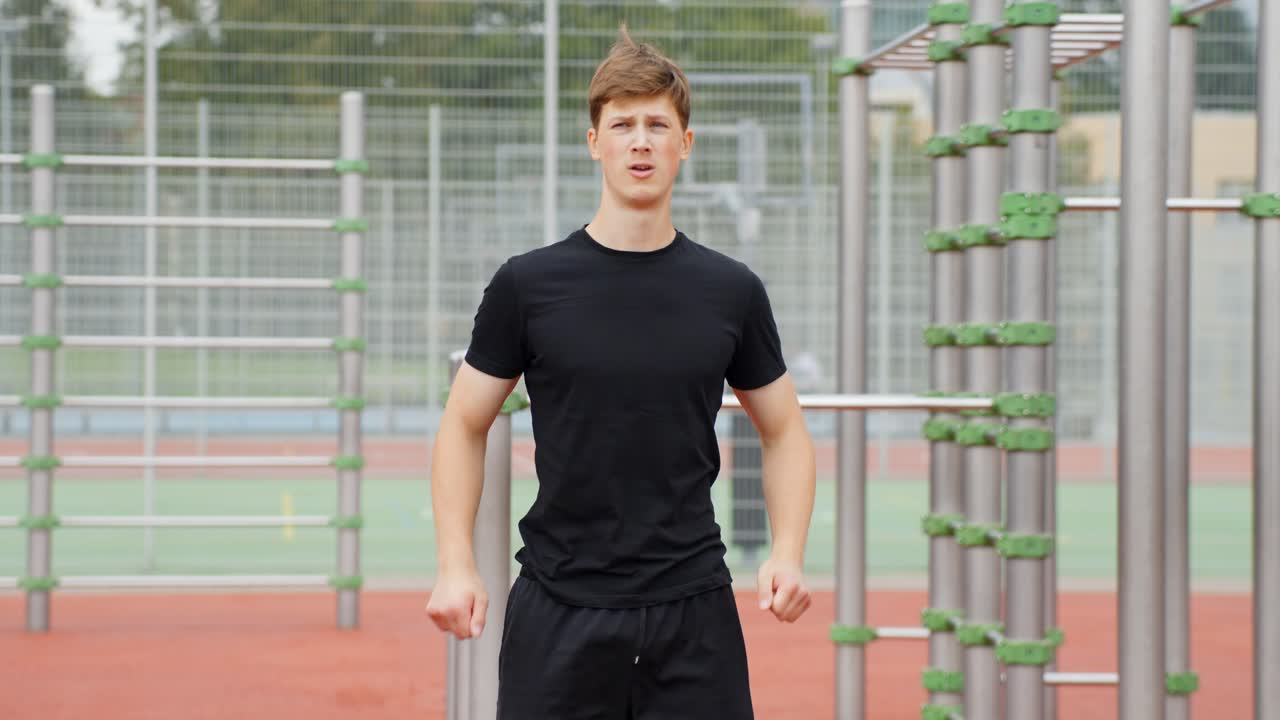Young man stretching his arm across his body, warming up his shoulder and arm muscles before exercising at an outdoor gym with metal bars, promoting fitness and health, static camera, slow motion