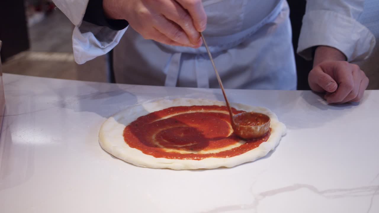 Uno chef aggiunge la salsa di pomodoro sulla pizza napoletana sul tavolo da cucina.