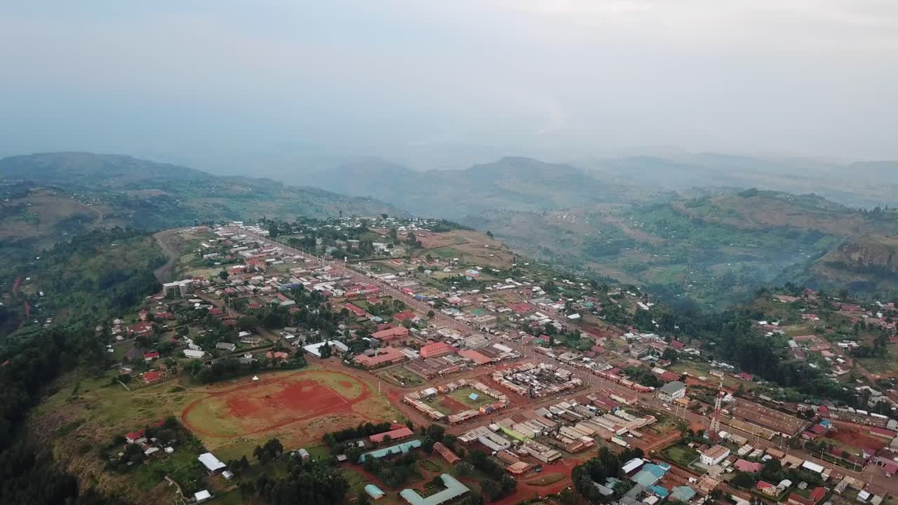 Wide drone view of Kapchorwa Town, Eastern Uganda, featuring a prominent red athletics track, surrounding buildings, and lush highland terrain on the slopes of Mount Elgon.