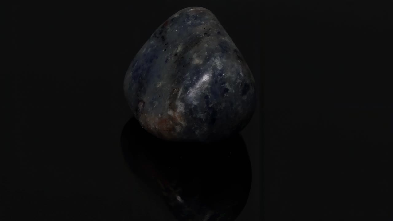 A detailed view of a polished blue stone resting on a glossy black surface, highlighting its texture and color variations.