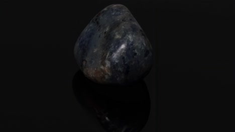 a detailed view of a polished blue stone resting on a glossy black surface, highlighting its texture and color variations.