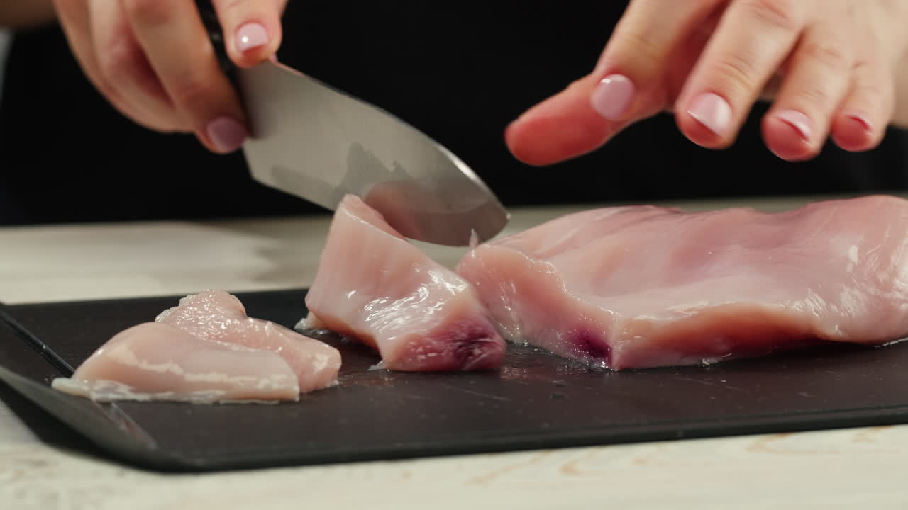 Man slicing raw turkey or chicken meat fillet on oak cutting board closeup, cooking with knife on restaurant kitchen. High quality 4k footage