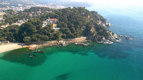 Stunning,-aerial-view-of-Fenals-beach,-green,-turquoise-transparent-water-El-Lloret-De-Mar,-Costa-Brava,-Tossa-de-Mar