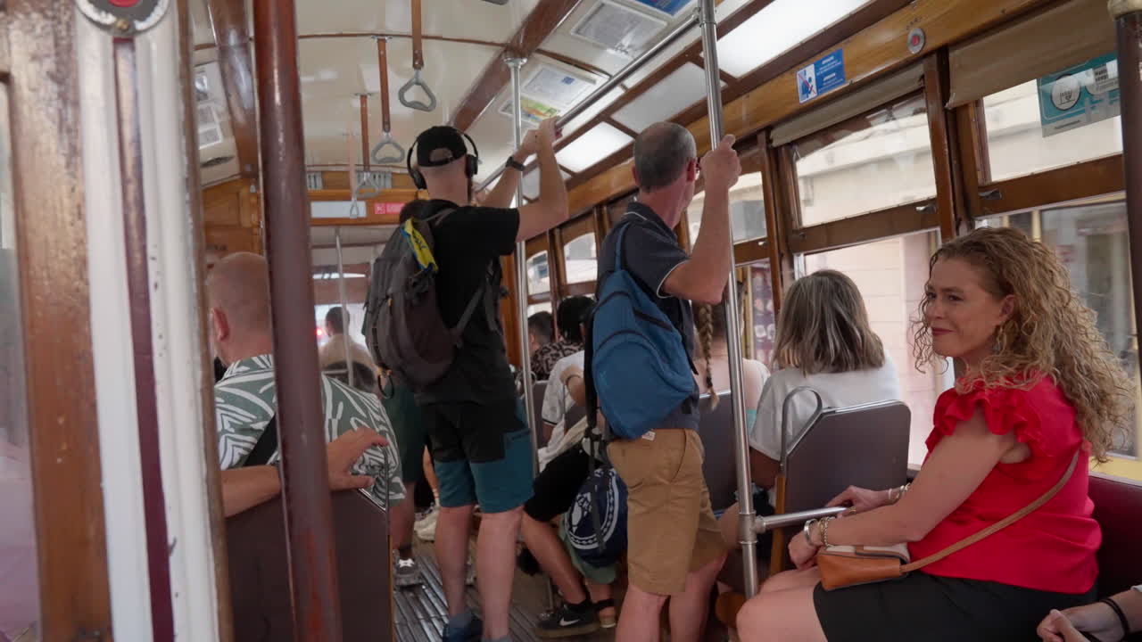 People casually transit in an electric trolley navigating the streets of Lisbon, Portugal, as passengers sit and hold onto the trolley, enjoying the ride through the city's historic landscape.