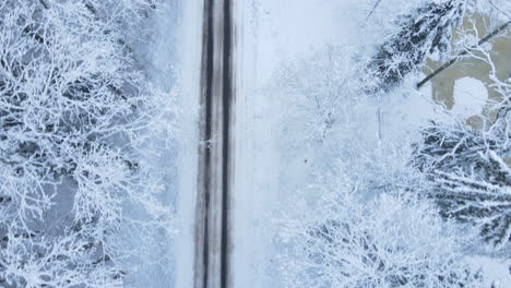 Top-Down-View-snow-covered-Forest-Road-in-winter,-Aerial-drone-back-movement-over-winter-road-low-hight-flying-close-to-the-frozen-tree-branches