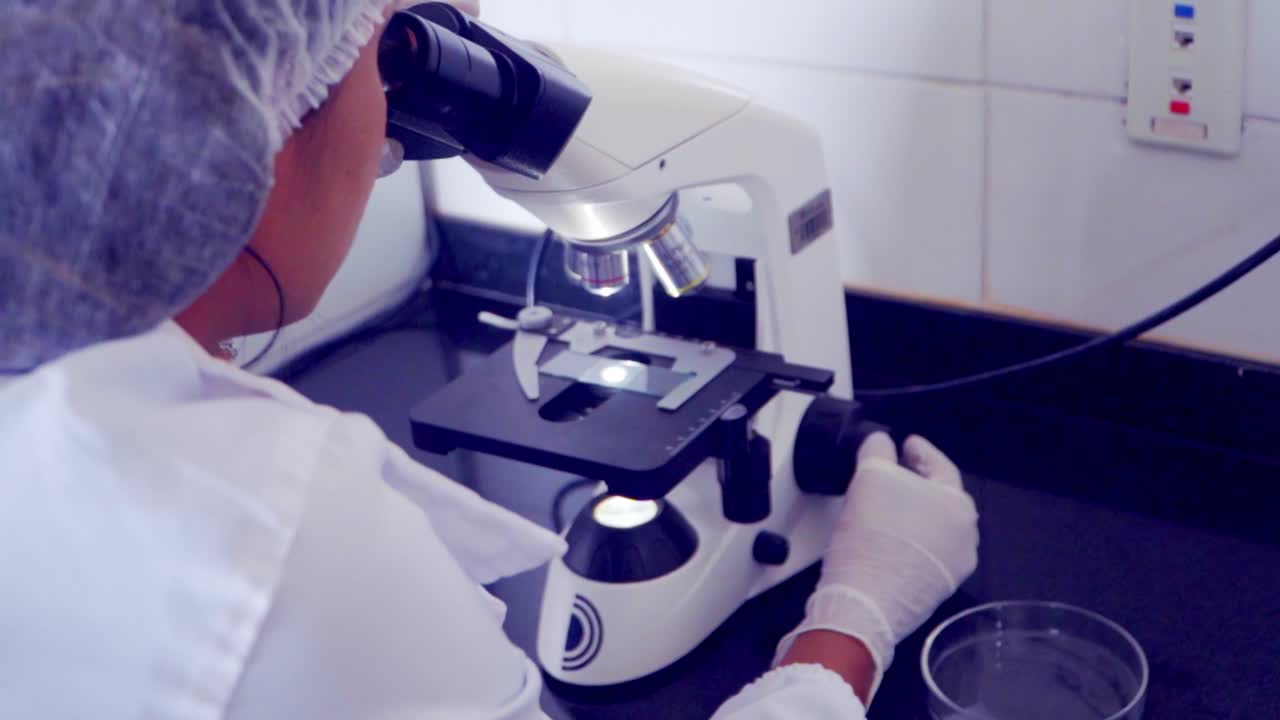 Scientist with safety equipment looking at a specimen under a microscope in a clinic. Medical research work