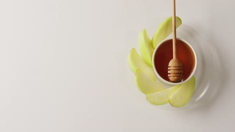 video of honey in jar and apple slices lying on white surface