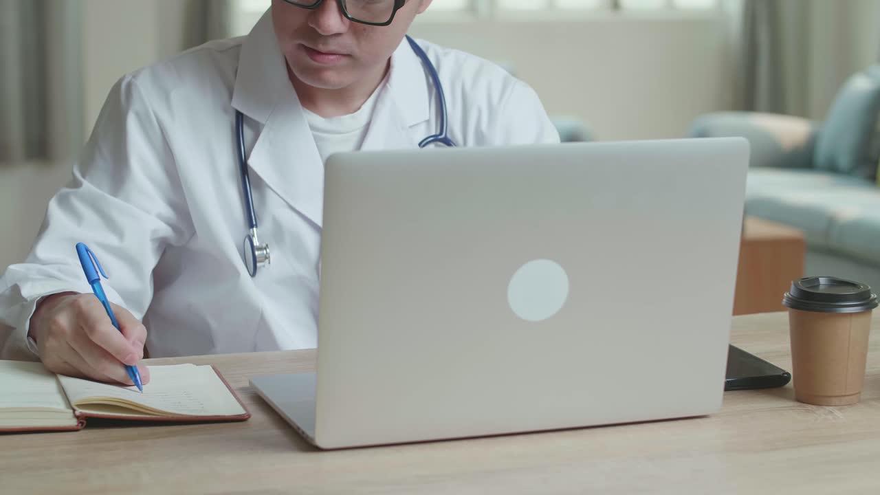 Male Doctor Working With Laptop And Writing On Notebook At Home Office, Video In 4K