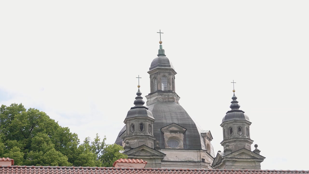 Imagens deslumbrantes em grande angular do histórico Mosteiro de Pažaislis em Kaunas, Lituânia. Cúpulas barrocas intrincadas, telhado de telhas vermelhas e árvores verdes exuberantes abaixo sob luz natural suave. Ninguém visível.