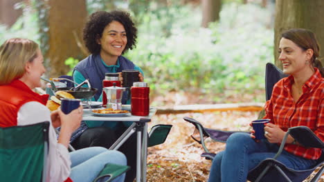 Gruppe-Von-Freundinnen-Im-Campingurlaub-Im-Wald,-Die-Gemeinsam-Am-Zelt-Sitzend-Essen-Kochen