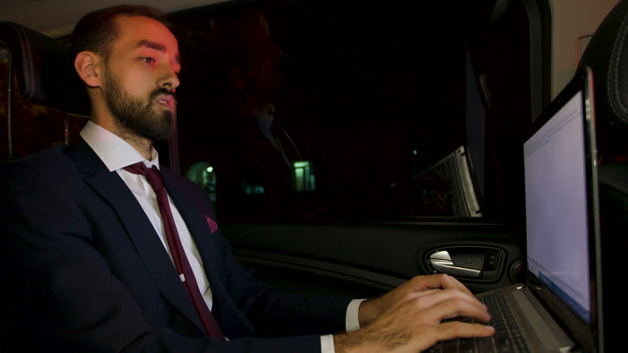 Uomo d'affari concentrato sul sedile posteriore di una limousine che digita sul laptop di notte