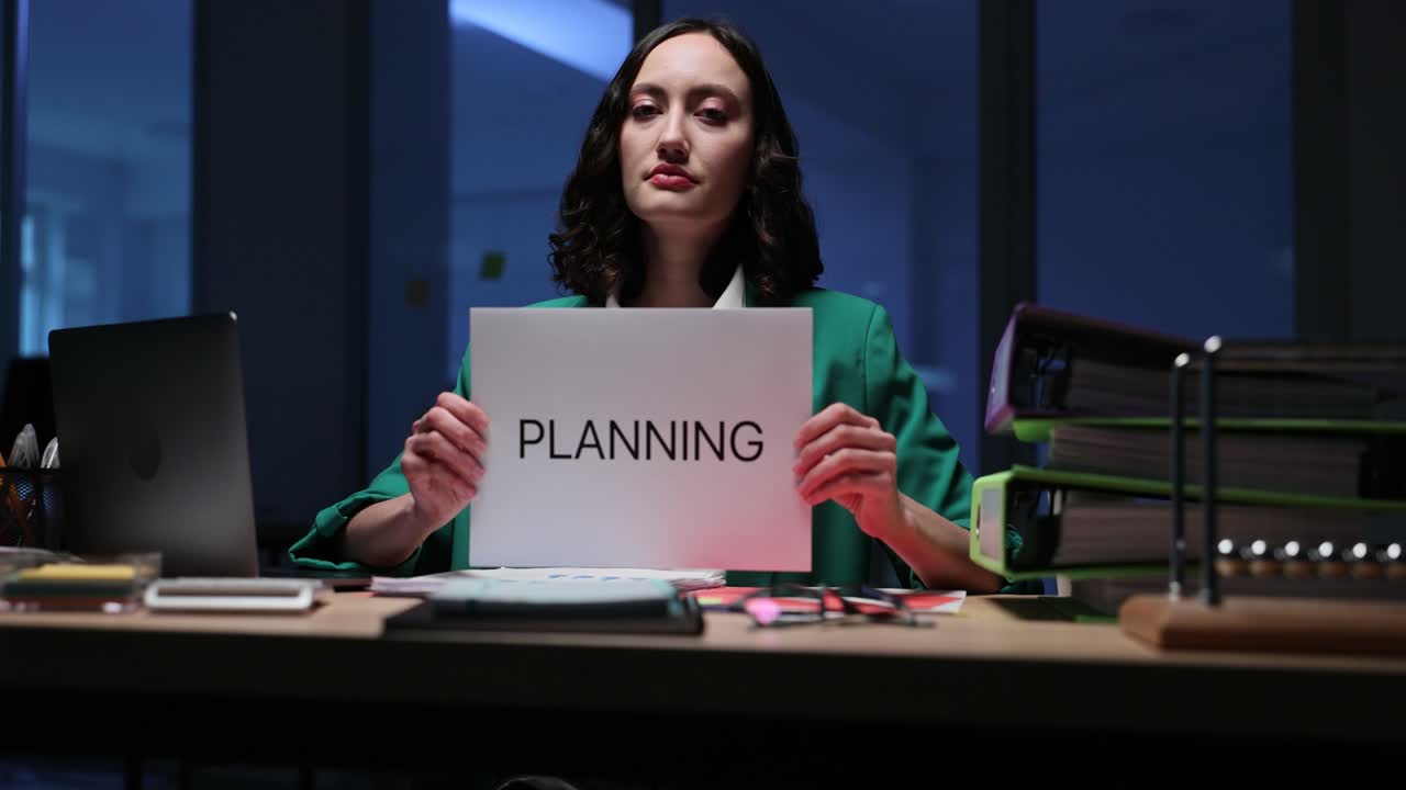 Woman holding a sign saying "Planning" at her desk