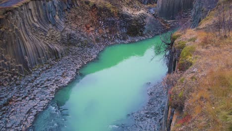 el agua del río turquesa en el cañón de studlagil con pilares de roca de basalto