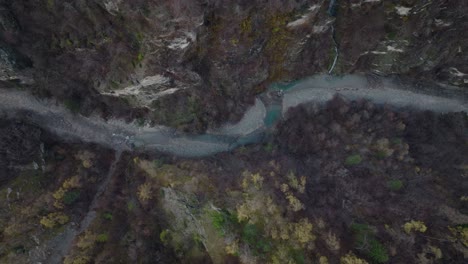 Entspannende-Luftdrohne-Von-Oben-Nach-Unten,-Seitliche-Aufnahme-Eines-Flusses,-Der-In-Einer-Stimmungsvollen-Winterlandschaft-In-Der-Schweiz-über-Eine-Alte-Brücke-Fließt