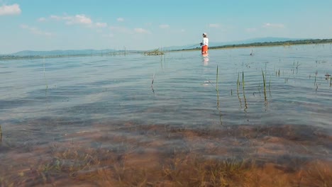 girl standing far away in a clear blue lake fishing on a sunny day