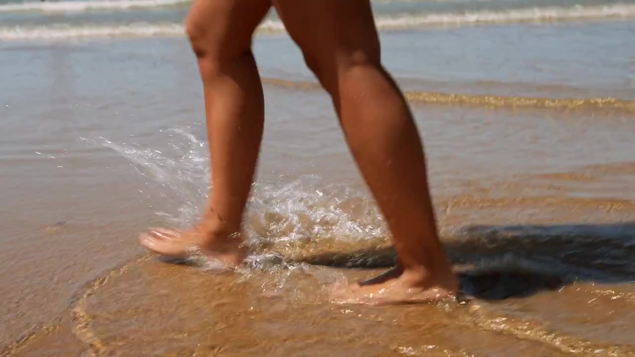 Primo piano di gambe che camminano e schizzano nell'acqua del mare sulla spiaggia