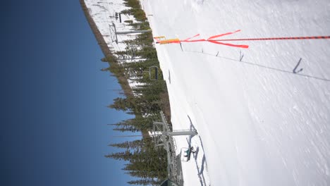 Ski-lift-carrying-passengers-up-a-ski-run-on-a-cloudless-day,-vertical