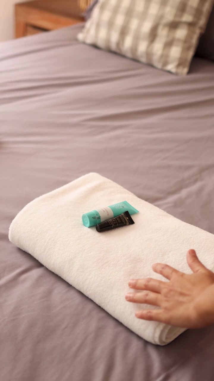 Mani sistemano un asciugamano e posizionano articoli da toeletta su un letto ben fatto con illuminazione soffusa.