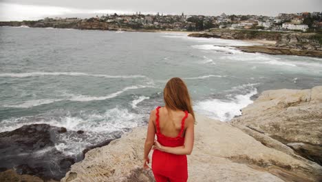 Chica-Vestida-De-Rojo-Camina-Descalza-Sobre-Las-Rocas---Chica-Parada-En-La-Roca-Observa-Las-Olas-Rompiendo---Suburbios-Del-Este,-Sydney,-Nsw,-Australia