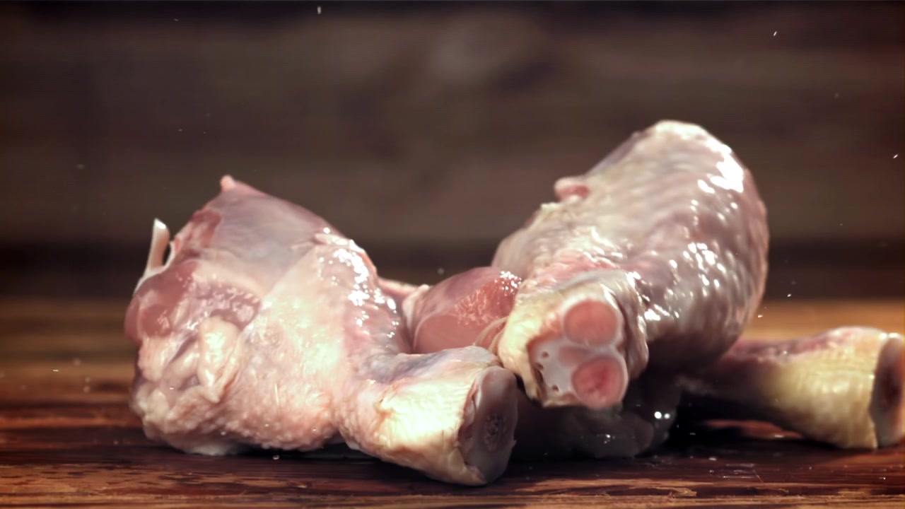 Fusi di pollo crudi che cadono su una superficie di legno in slow motion