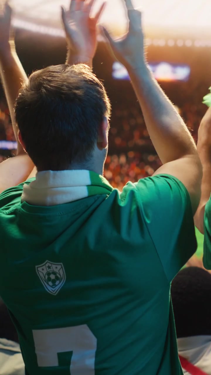 Video vertical Aficionados al fútbol con camisetas verdes aplaudiendo y animando desde las gradas del estadio