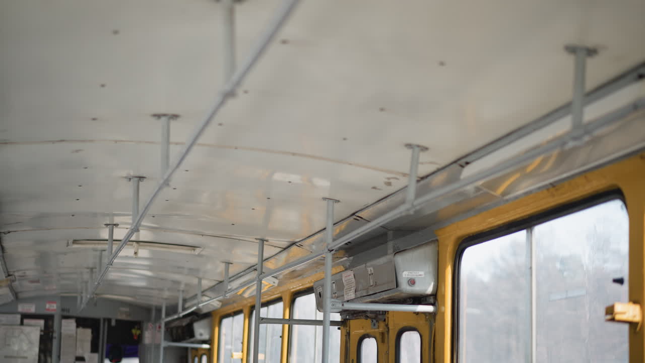 upward interior view on moving bus shows ceiling rails, poles, yellow window frames, frosted glass, metal fixtures, winter city sliding past outside, calm urban commute mood with soft daylight